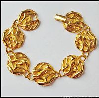 Full top-down view of the gold tone link bracelet with textured and smooth swirl pattern and fold over clasp.