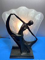 Front view of bronze finish flapper figurine and illuminated frosted glass shade with peacock feather design