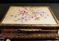 Closed view of the petit point jewelry box showing detailed floral embroidery and ornate brass-toned edging.