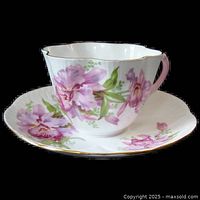 Side angle showing the cup with fluted rim, pink handle, and large pink orchid floral design; matching saucer with floral detail and gold trim.
