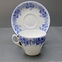 Cup and saucer set positioned with cup in front and saucer behind showing floral patterns and gold-trimmed handle on cup.