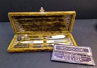 Open antique green velvet sewing tool box showing included tools and needle packet.