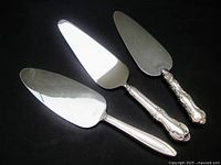Three cake/pie servers with sterling silver handles and stainless steel blades placed on black background.