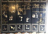Front view of 6-panel vintage Chinese black lacquered screen with gold floral detailing and inlaid mother-of-pearl borders, showing colored stone figures and inset musical instrument panels along the bottom.