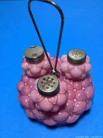 Pink bubble glass condiment set with metal handle and three containers on blue background.