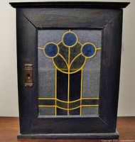Front view of the vintage wooden cabinet showing stained glass door with blue circular designs and lock plate.