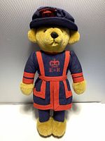 Front view of the vintage teddy bear wearing the blue Beefeater uniform with red accents, showing embroidered crown and E II R letters.