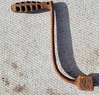 Full view of antique cast iron shaker ash grate handle showing L shape, holes on handle, and rust wear
