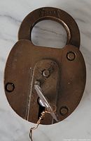 Front side of the antique Fraim brass padlock showing the embossed 'FRAIM' logo and keyhole with the key inserted.
