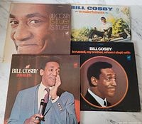 Four vintage 1970s Bill Cosby comedy vinyl albums, front covers visible, showing portraits of Bill Cosby and album titles such as Its True! Its True!, Wonderfulness, 200 M.P.H., and To Russell, My Brother, Whom I Slept With.