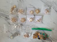 Top-down image showing multiple brooches individually bagged and a zip-lock bag containing assorted colorful costume gems.