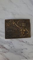 Front view of the brass belt buckle showing detailed relief of nude woman and Coca Cola text.