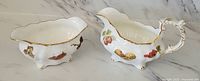 Side view of cream and sugar set showing fruit decorations and gold trim on white bone china
