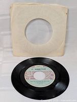 Full image of the black 45 RPM record with original white sleeve, showing condition and label.