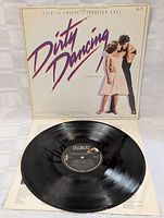 Front view of the vinyl record partially out of its cover showing label and grooves.