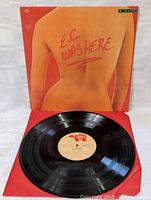 LP vinyl record partially removed from sleeve displaying clean black vinyl and centered beige label with red text.