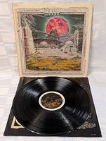 Vinyl record taken out showing black disc and label on turntable with album cover behind.