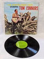 Front view of album cover with Stompin' Tom Connors holding guitar standing by driftwood log outdoors.