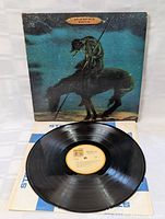 Vinyl record laid flat in front of its album cover, showing the record's surface and label