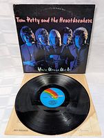 Vinyl record resting on a beige surface with the album cover standing upright in the background. Record has a multi-color MCA Records label at the center. Black vinyl appears clean and without visible scratches.