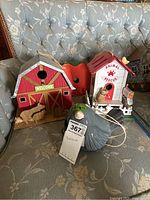 Red barn-shaped birdhouse, white animal rescue house, ceramic bird-shaped birdhouse, and orange apple-shaped birdhouse on floral couch