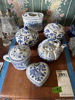 Photo showing all six blue and white porcelain items: two lidded jars, teapot, mug, heart-shaped trinket box, and toothbrush holder on wooden surface