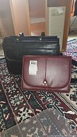Black USL laptop briefcase and burgundy leather-like portfolio folder placed on a patterned rug in front of wooden furniture and computer tower.
