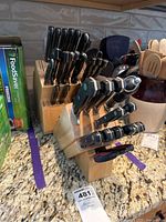 Photo of two wooden knife blocks with multiple black-handled knives stored, laid out on granite countertop beside kitchen items.