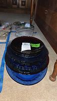 Stack of assorted colored Depression glass plates and bowls in blue tones ranging 8-16 inches.