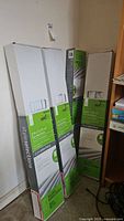 Four sealed boxes of white 2-inch faux wood blinds from Style Selections leaning against a wall.