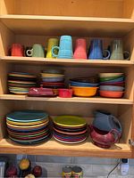 Cabinet shelf with assorted Fiestaware mugs, stacks of multicolor plates and bowls