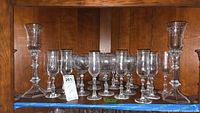 Shelf of Fostoria stemware and two candlesticks showing various glasses with clear and etched glass patterns, different sizes from about 5 to 8 inches tall