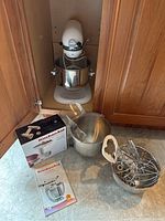 Overview of mixer, bowls, attachments, manual, cover, and boxed food grinder attachment on floor