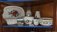 Shelf with assorted Lenox, Noritake, Wedgewood, and Christmas-themed dishes including plates, bowl, basket, and container.
