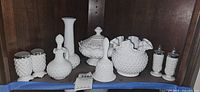 Shelf with milk glass collection including hobnail vases, a bell, a lidded dish, and a ruffled edge bowl.