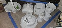 Overview of the milk glass items arranged on the floor showing various pieces including lidded dishes, basket, shakers, and bowls.
