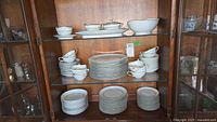 Shelf with neatly stacked porcelain plates, bowls, cups, and saucers, showing size range and quantities