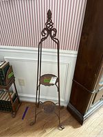 Full view of the metal plant display stand showing two round shelves and decorative top scrollwork. Shows signs of rust and wear.