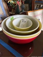 Four nesting Pyrex mixing bowls of different colors on a table with various items in background.