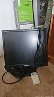 Front view of Samsung SyncMaster 712N monitor with cables coiled beside it, showing screen and stand.