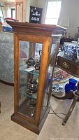 Small wooden curio cabinet shown from angle, displaying glass panels and door with brass handle.