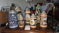 Wide shot showing grouping of vintage German steins with varied sizes and designs on wooden surface