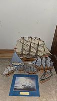 Photo showing large tall ship model with white sails, smaller striped sailboats, and flat unframed print lying on carpet