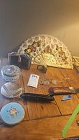 Lot overview including compact powder cases, hand fan, glasses and miniature frames on wood table