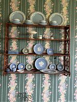 Full view of shelving unit displaying Wedgewood plates, cups, cake pedestal, ashtrays, and lighter.