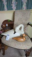 Both wooden duck figurines displayed on a floral upholstered chair, showing size difference and finish details.