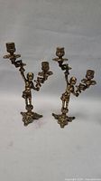 Two brass candlesticks featuring boys holding two torchere candle holders each, standing on ornate bases.