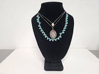 Front view of two fine silver chain necklaces with teardrop pendants and turquoise bead necklace with large oval pendant on black display bust.