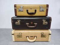 Three vintage suitcases stacked, two beige/cream and one black, showing overall size and condition