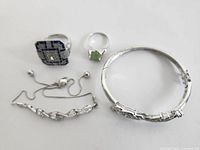 Photo showing 3 rings and one bracelet laid flat on a white surface. The bracelet has a linked design and the rings feature different stones including blue, clear, and green crystals.